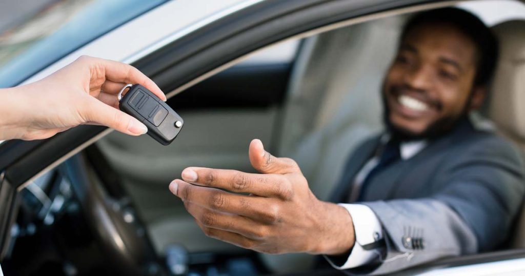 Professional salesperson handing over car keys to a delighted new car owner with a big smile and an approved car loan.