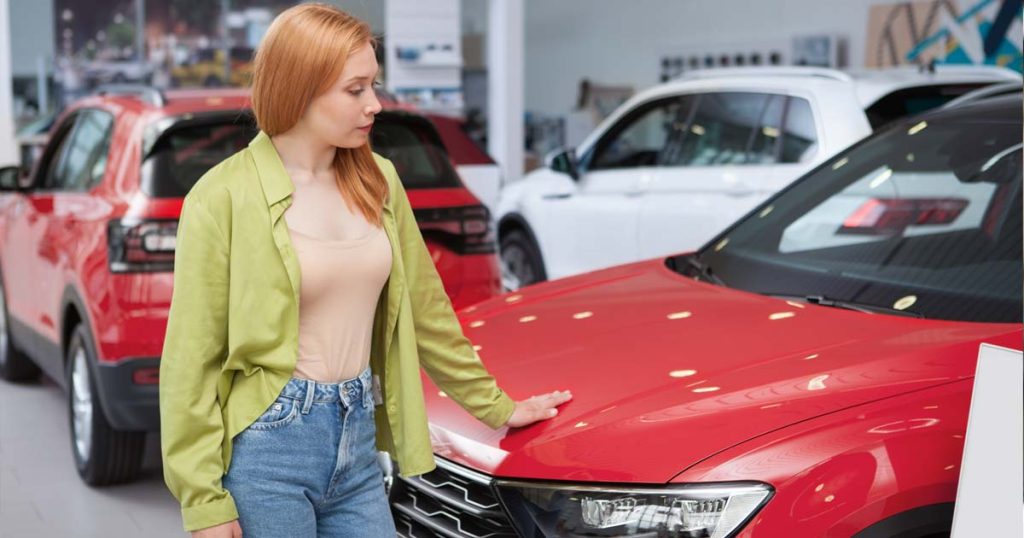 Young woman examining new cars at a dealership, considering an auto loan.
